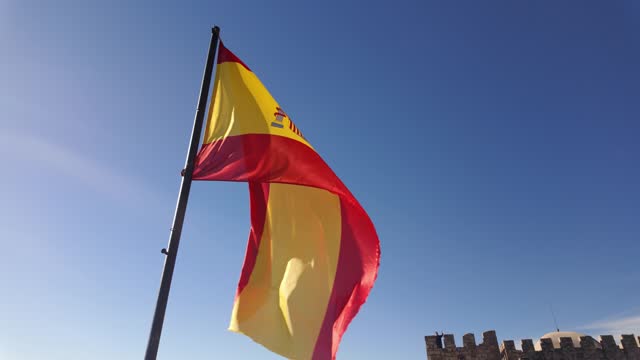 Spanish flag waving in the wind in slow motion with the sun shining in the blue sky, Trujillo