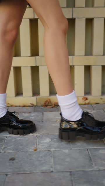 Trendy Footwear and Socks on Urban Pavement. A close-up of a person's legs in stylish black shoes and white socks, standing on a cobblestone path.