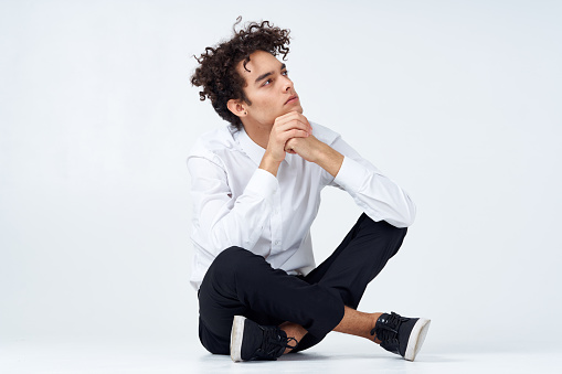 guy with curly hair in a white shirt, sneakers and trousers sits on the floor. High quality photo