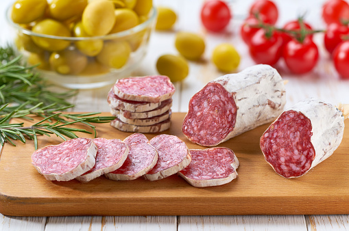 Traditional Spanish fuet spicy pork dry cured salami sausage with rosemary and baguet on a wooden table.