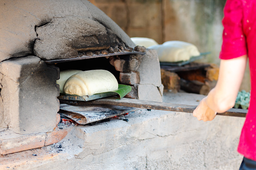 Placing bread dough to bake in a rustic wood-fired oven. The image depicts the traditional way of making and baking homemade bread in the Brazilian countryside