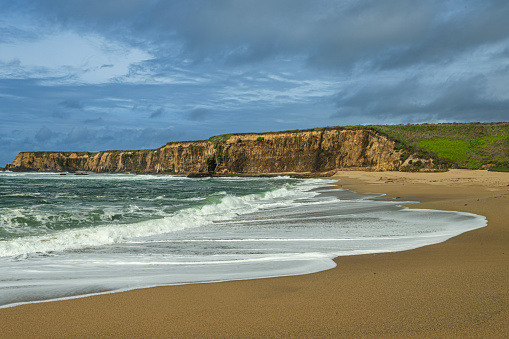 Turbulent ocean waves breaking along the Pacific coast under a cloudy sky, as a storm passes through the area.\n\nTaken in Davenport, California, USA