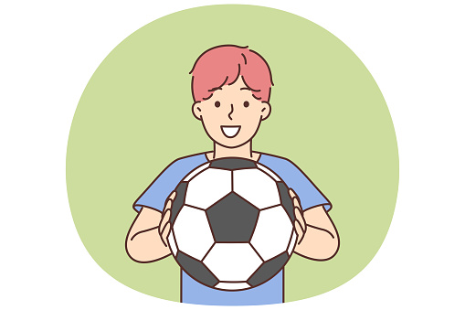 Cheerful boy of school age holding soccer ball and smiling offers to play football. Positive boy football player dreams of becoming professional sportsman and participating in premier league