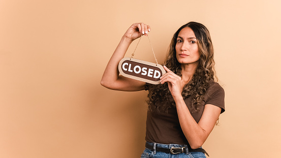 Brown background of a woman holding and pointing to the close sign of an space