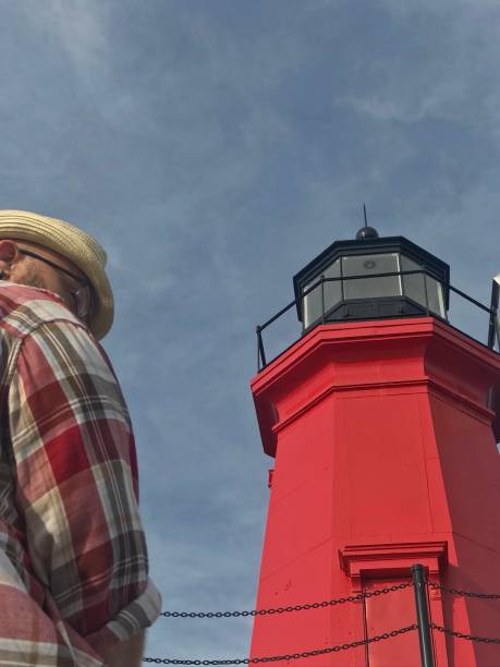 Mature bearded man in a straw hat and flannel shirt standing on a lighthouse pier outdoors. The man is suffering from young onset dementia including Alzheimer’s and frontal lobe. The lighthouse pier is on Lake Michigan  in Menominee, Michigan.