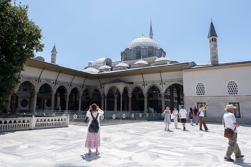 tourists visiting the inner courtyard of the imperial palace of topkapi, an asian tourist takes a picture of the building with her mobile phone, horizontal