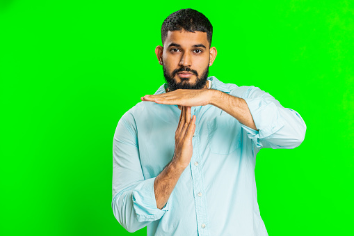 Tired serious upset Indian young man showing time out gesture, limit or stop sign, no pressure, I need more time, take a break, relax, rest, help. Arabian guy isolated on green chroma key background
