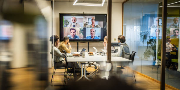 Business people attending a hybrid presentation Business people attending a hybrid meeting with some people in a conference room and others attending via video conferencing on a large screen. conference call stock pictures, royalty-free photos & images