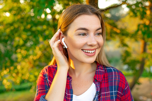 Happy young woman with smartphone listening to music through wireless earphones on green background