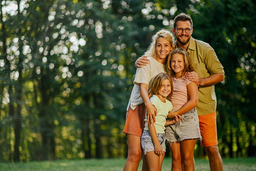 Portrait of loving parents standing in nature with their children and spending free time outdoors. An affectionate family standing on meadow near forest and posing for a family portrait. Copy space.