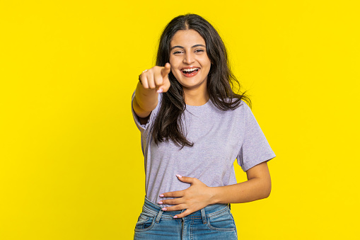 Happy Indian young woman laughing out loud after hearing ridiculous anecdote, reaction on funny joke, feeling carefree amused. Positive people lifestyle. Arabian girl isolated on yellow background