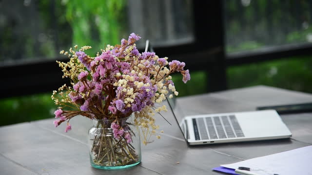 Office decoration flower bouquet with a laptop on wooden table. pink pastel flower on grass vase office supply with copy space