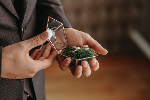 Wedding gold rings on a decorative glass box with wooden green moss, standing in the hands of the groom, close-up. Jewelry concept