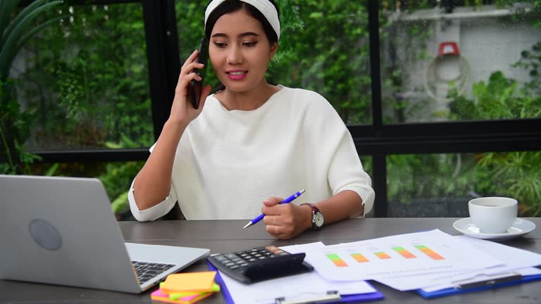 Asian women talk via smartphone work from home small office desk. Young asian Woman hands holding phone technology lifestyle. Happy Women person calling use digital smart phone working home office