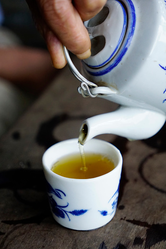 Close up photo of a man pouring tea from a ceramic teapot to matching cup
