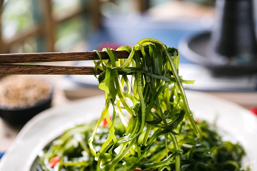 High angle view of an anonymous Asian female chef holding nori seaweed sheets and preparing a healthy meal at home.