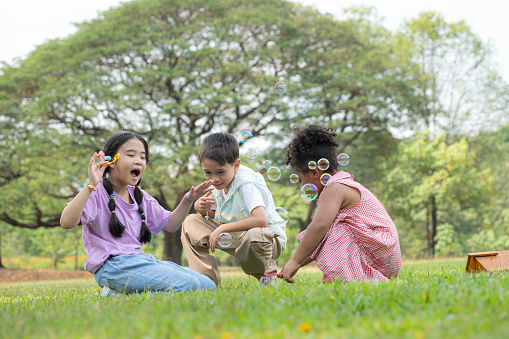 Children sitting in the park with blowing air bubble, Surrounded by greenery and nature