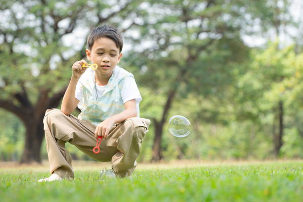 Boy sitting in the park with blowing air bubble, Surrounded by greenery and nature