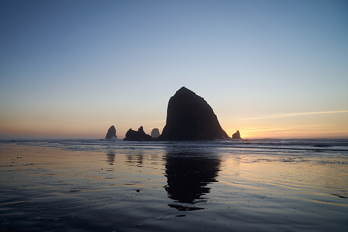 Cannon Beach at sunset: where the sky ignites in hues of orange and pink, Haystack Rock stand tall, and the waves create a serene ambiance, captivating all who witness this natural masterpiece.
