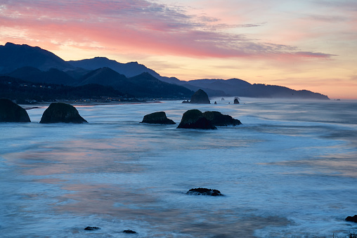 Cannon Beach at sunset: where the sky ignites in hues of orange and pink, Haystack Rock stand tall, and the waves create a serene ambiance, captivating all who witness this natural masterpiece.