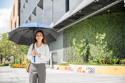Walking to the office on a scorching day, a young businesswoman holds an umbrella to shield herself from the hot sun. Her determination and sweat highlight her commitment to success.