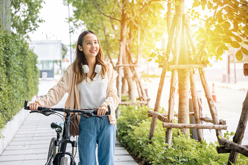 Lifestyle Asian young woman walking alongside with bicycle on summer in countryside outdoor, Happy female smiling walk down the street with her bike on city road, ECO environment, healthy travel