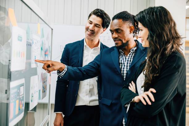 istock Colleagues meet in the office, using sticky notes on a glass board for brainstorming. This diverse group exemplifies teamwork, leadership, and effective solutions in business discussions. 2057154805