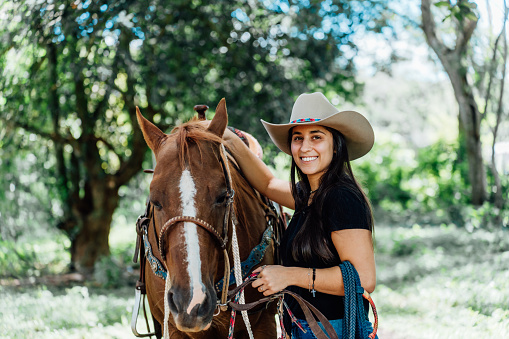 Portrait of a smiling cowgirl preparing her horse