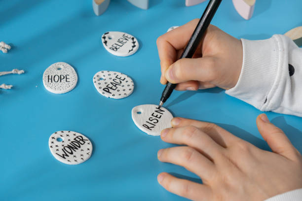 istock Master class writing word RISEN on EASTER clay egg Unrecognizable artist do it yourself air dry clay crafts for Easter holiday. Decoration gift idea Handmade children craft. Step by step instruction of painting, pressing figures 2057162543