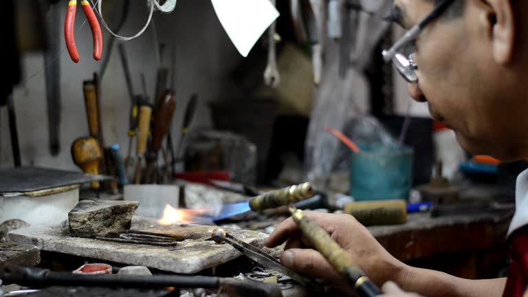 Jeweler, goldsmith in a professional jewelry workshop uses a burner to create a metal ring at a jewellery workshop.