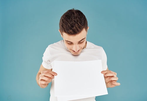 Male advertiser with a white sheet of paper on a blue background mockup Flyer. High quality photo