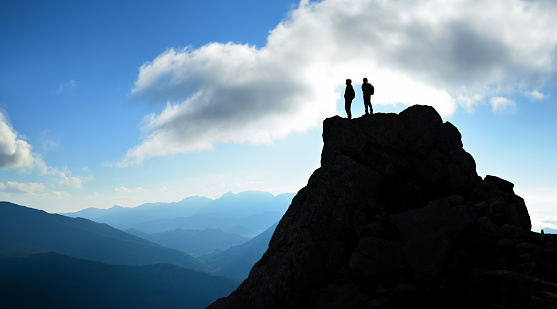 Two climbers watching the surroundings on the cliff at the summit and the serenity of victory