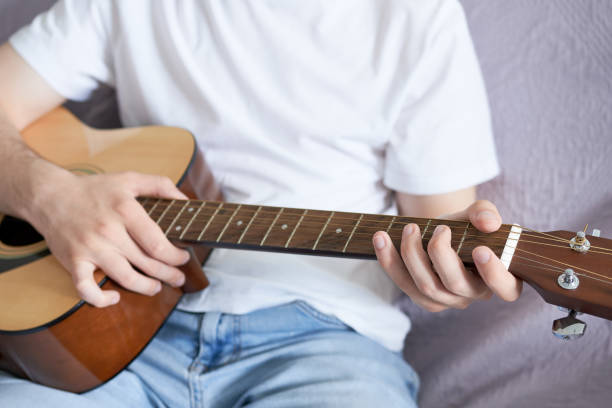 istock Young man holding a guitar while sitting on a couch in a room. Learning to play the guitar. 2057242406