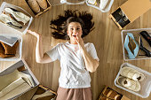 Woman surrounded by shoes in plastic container and cardboard box shopaholism and storage organizing
