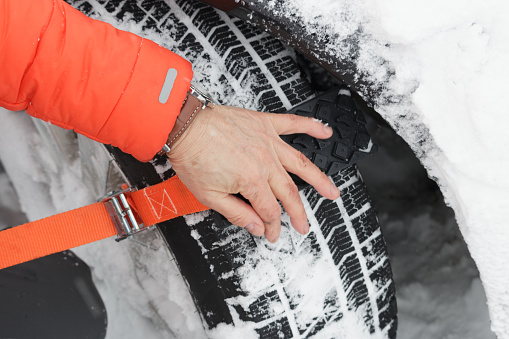 Senior Japanese male attaching a temporary snow chain to a winter tyre