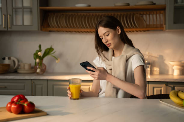 istock Young Woman Texting on Smartphone at Kitchen Counter During Morning Hours 2057348491