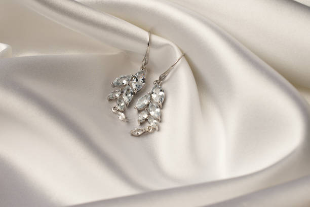 istock Silver earrings with diamonds on beige silk background 2057354423