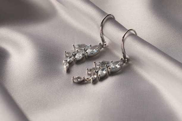 istock Silver earrings with diamonds on beige silk background 2057354425