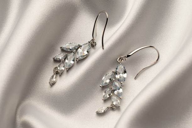 istock Silver earrings with diamonds on beige silk background 2057354427