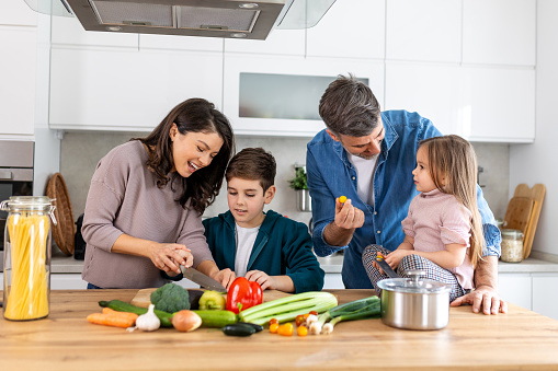 Happy family cooking together on kitchen. Mother Son and daughter with father cooking. Son and mother chopping green vegetables. Home recreation and food preparation on weekend