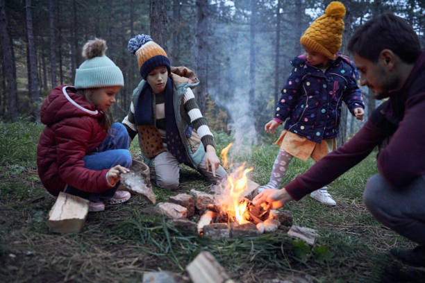 Beautiful children and single father are spending time together near a campfire in the wood.