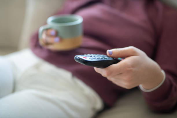 Young woman with a cup of coffee relaxing and watching TV at home.