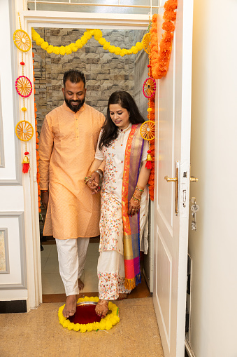 Happy indian couple of entering new house for the first time. both husband and wife stepping in a plate filled with liquid kumkum. Griha Pravesh Concept
