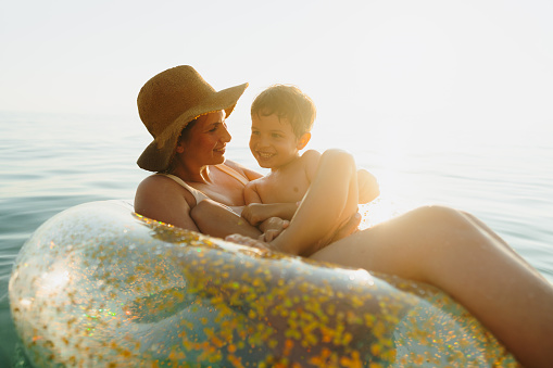 Photo of a young boy and his mother, relaxing and cooling off in the ocean on a hot summer afternoon, using the inflatable ring as a raft