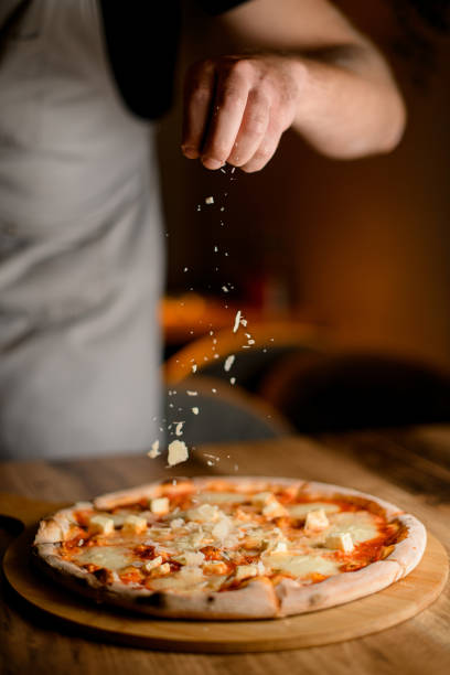 istock Man in gray sprinkles cheese on pizza on a wooden table in a kitchen 2057465855