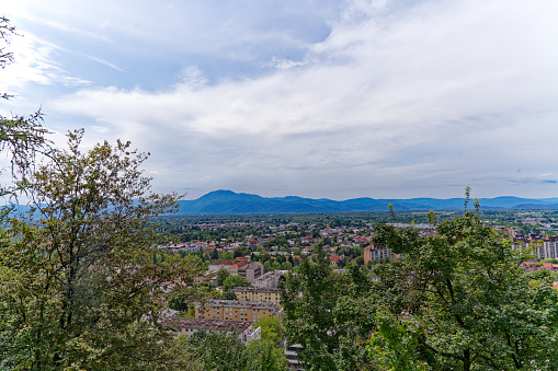 Aerial view of City of Ljubljana seen from castle hill with skyline and mountain panorama in the background on a cloudy summer day. Photo taken August 9th, 2023, Ljubljana, Slovenia.