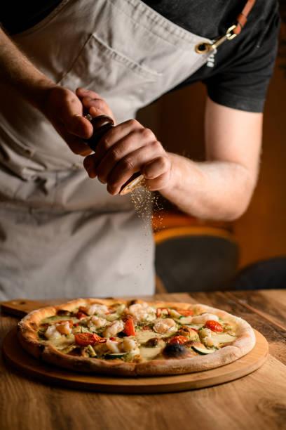 istock Pizza man sprinkles spices on pizza on a wooden table in a kitchen 2057481200