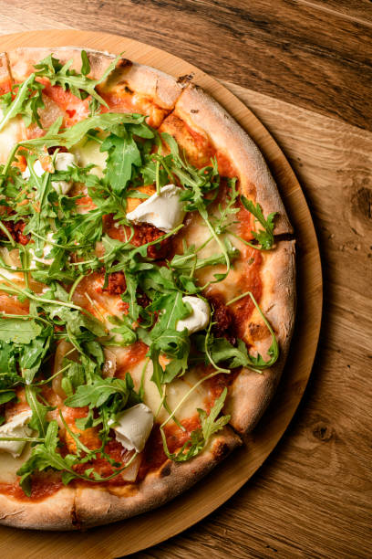 Juicy cheese pizza with arugula and herbs, mozzarella and cream cheese on a round wooden stand on a table