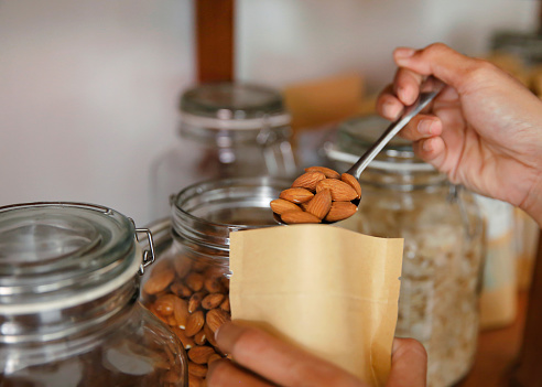 Close-up POV shot of unrecognizable customer hand inserting one tablespoon of roasted almond nuts into a sealed brown paper bag. Concept : self service organic food store.