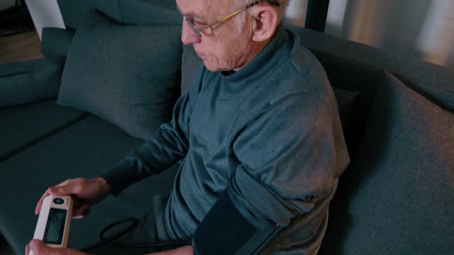 Senior man puts on a blood pressure cuff and looks at his blood pressure readings
